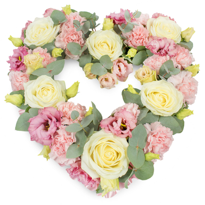 This image shows a meticulously crafted, heart-shaped floral tribute, photographed against a smooth white background so every pastel detail is clearly visible. The heart is completely filled, without gaps, giving a sense of abundance and care. At its core are generous cream and pale yellow roses, their petals arranged in tight spirals that gradually loosen towards the edges, each bloom like a quiet promise of enduring affection. Between them, clusters of ruffled light pink carnations provide soft volume, their many-layered petals creating a gentle, almost feathery texture reminiscent of folded fabric. Deeper mauve and magenta-pink lisianthus blossoms are scattered thoughtfully throughout, some just opening, others fully unfurled, adding a romantic depth of colour that subtly draws the eye around the heart. Silvery-green eucalyptus leaves thread their way through the flowers, their rounded shapes and matte finish lending a cool, calming contrast and clearly tracing the curve of the heart from top to pointed base. Tiny yellow-green buds appear here and there, adding small sparks of freshness and suggesting that the flowers were arranged only hours before, ready for same-day delivery to a remembrance service in Shacklewell or a nearby chapel in Dalston. The overall composition feels balanced, symmetrical, and intentional, reflecting the steady hands and experience of a local florist. Emotionally, the wreath conveys tenderness, sympathy, and gratitude, making it an appropriate tribute for funerals, memorials, or anniversaries when families in the Shacklewell community wish to honour a loved one with a symbol of love that feels gentle yet deeply sincere.